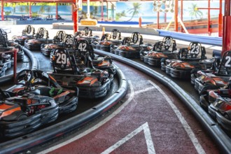 Rows of empty go karts lined up on an indoor race track, engines idle, safety barriers hugging the