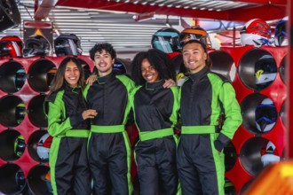 Happy diverse friends smiling, wearing green racing suits, standing together in a karting facility