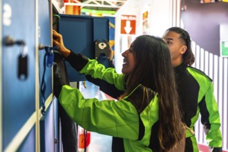 Young woman smiling while reaching into a locker to retrieve gear, with a man standing beside her,