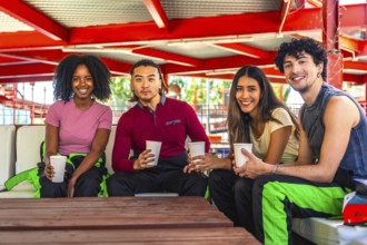 Multiethnic group of young adults in racing suits relaxing at a table with drinks, smiling and