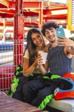 Young couple wearing racing suits taking a selfie during a karting break, showing happiness and