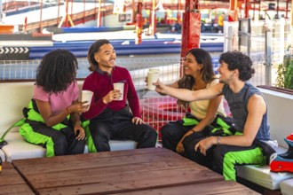 Group of diverse young adults wearing racing suits sitting on a couch, laughing and toasting each