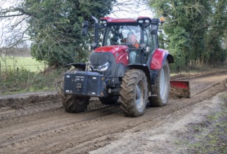 Tractor grading and levelling work repair a muddy, flood-prone country lane, Sutton, Suffolk