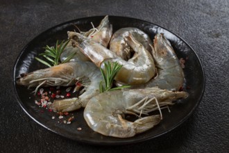 Fresh raw white-footed shrimp, tiger prawns vannamei, on a black plate, with spices and herbs