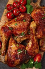 Grilled fried chicken legs, served with fresh cherry tomatoes, and herbs, on a wooden chopping
