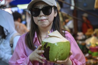 Mae Klong, Thailand. March 15th 2025. A smiling tourist with fresh coconut juice at the Mae Klong