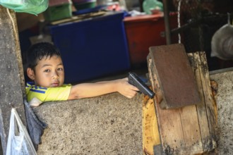 Mae Klong, Thailand. March 15th 2025. A young Thai boy with a toy gun at the Maeklong Railway