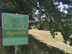 A green signpost, watershed, Wurmloh Pass, on a sunny meadow under a tree, Franconian mountain