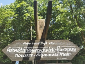 Wooden sign with the inscription Watershed North Sea, Black Sea, in an area surrounded by trees,