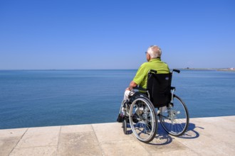 Senior in wheelchair looking at the sea, vacation with a handicap, Grado, Julian-Friuli, Adriatic
