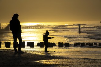 Winter on the North Sea, sunset at sea, beach walkers, coastal protection, through wooden posts,