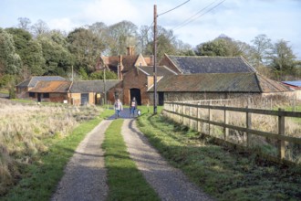 Two people walking a dog on country lane track near farm buildings at Martlesham Wilds, Suffolk,