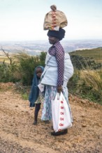 Woman with child and bay on her back, carrying a load on her head, standing in rural area, South