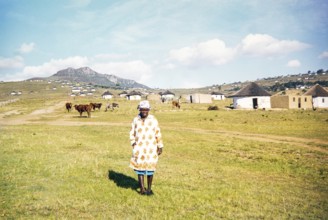 A local woman stands in the foreground of a rural Xhosa village (umuzi) in the Eastern Cape, South