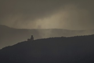 The structure is on a mountain. The sky is cloudy and sunlight is shining in the distance. The