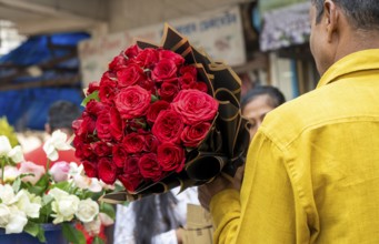 A customer holds a bouquet of red roses at a flower shop on Valentine's Day in Guwahati, India, on