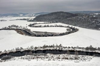Snow-covered fields with a gently rolling river, surrounded by hills and trees in cloudy skies, The