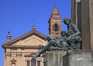 Monument with a statue in Piazza Unita and the Santo Stefano Collegiate Church in the city of