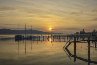 Atmospheric sunrise scene with calm water and sailboats on the jetty, Lake Constance, Überlinger