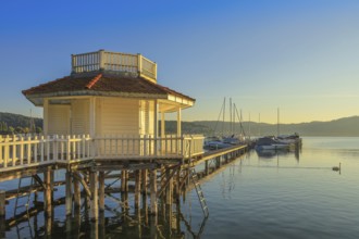 A pavilion on a jetty stretches across Lake Überlingen, with boats and mountains in the background