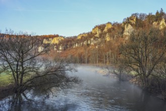 Picturesque river landscape with foggy water, surrounded by autumn trees and imposing Jurassic