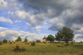 A small chapel stands on a green hill under a cloudy sky with trees, Upper Danube nature park Park,