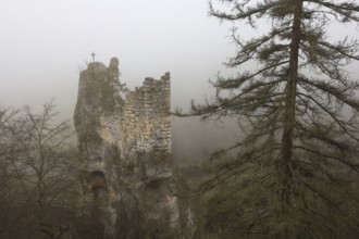 An abandoned castle ruin in fog with a cross on the tower, surrounded by trees and an autumnal