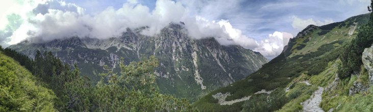 A trail leads through impressive mountain scenery, panoramic peaks covered with green slopes and