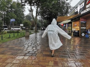 Person in raincoat with Zakopane inscription walking on wet sidewalk in rainy weather, Zakopane,