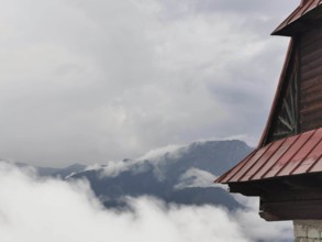 View of a mountain peak through clouds, with part of a wooden building in the foreground, Zakopane,