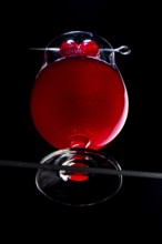 A cognac glass with red liquid and cherries, dramatically illuminated, view from below