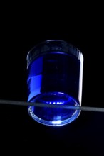 A glass with blue liquid against a black background, dramatic lighting