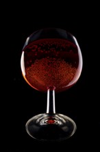 A wine glass filled with sparkling red wine against a black background