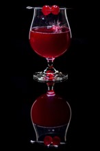 Cherry falls splashing into a cognac glass with a red drink against a dark background and