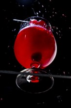 Sparkling red drink with cherries in a cognac glass on black background, view from below