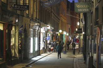 Busy street with pedestrians and illuminated shops at dusk, Gamla Stan, Old Town, Stockholm, Sweden