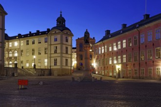 An illuminated town square with historic buildings and a memorial at dusk, Riddarholmen, Stockholm,