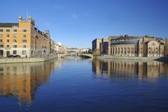Clear river water with reflecting buildings and a bridge under a blue sky, Government District,