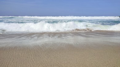 Empty sandy beach with breaking waves under clear blue skies, hiking on the Fisherman's Trail,