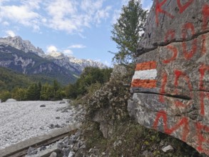 Rock with red and white markings, hiking trail, and mountain views under blue sky and clouds, Peaks