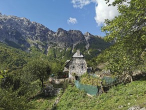 Stone house surrounded by gardens and mountains under a clear blue sky, Peaks of the Balkans,