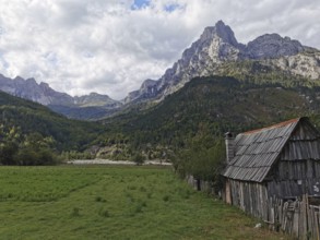 Small wooden cabin in a grassy willow with majestic mountains in the background, Peaks of the