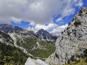 Rugged mountain landscape with clouds and blue sky, trees on rocky hillside, Peaks of the Balkans,