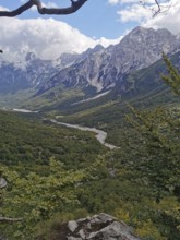 Wide view of a green valley with a river and high mountains under cloudy sky, Peaks of the Balkans,