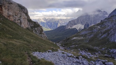 View of a rocky valley surrounded by imposing mountain ranges under a partly cloudy sky, Peaks of