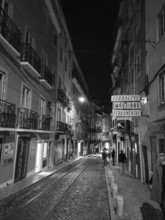 Nighttime street scene in a city with illuminated signs, tram tracks and people walking by,