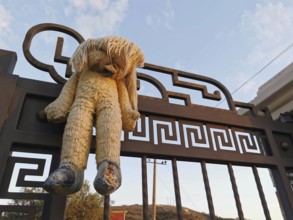 An old plush bear hangs abandoned on a rusty, metal gate at dusk, Himare, Albania