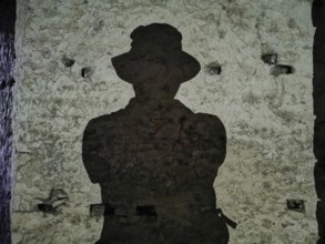 A dark shadow silhouette of a person wearing a hat on an old stone wall, Albania