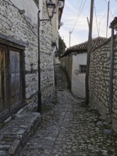 Narrow, cobblestone alley with old stone walls and traditional houses, old town of Berat, Albania
