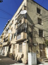 Old, yellowed building cluttered with power lines with numerous satellite dishes and cables in the
